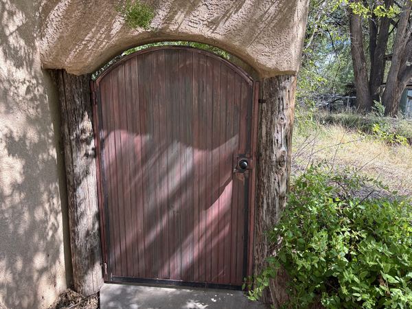 Arched gate with a weathered red-brown patina finish set into a stucco archway