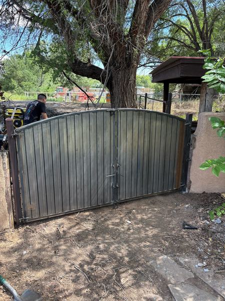 Arched double steel gate in progress under a large tree