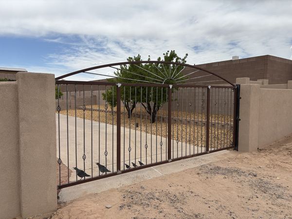 Brown steel swinging driveway gate with a sunburst arch and twisted pickets