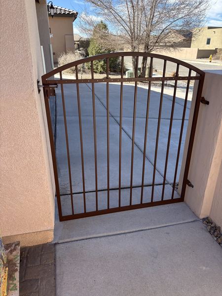 Bronze-colored arched picket pedestrian gate between stucco walls