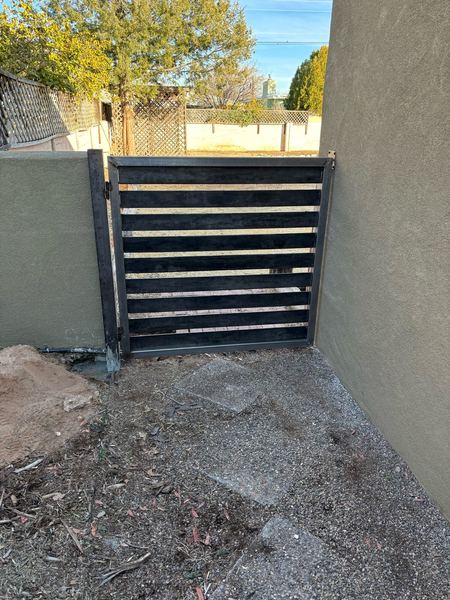 After: black horizontal-slat steel pedestrian gate between two walls