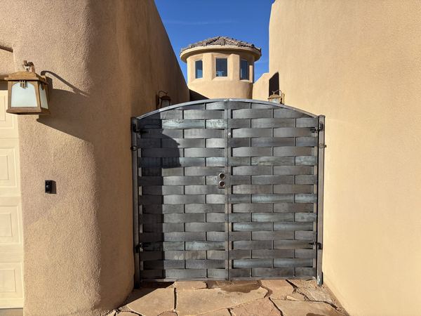 Arched double gate of woven flat steel strips between stucco walls